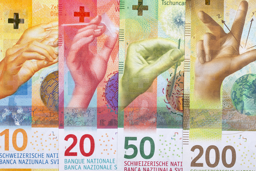 Close-up of four Swiss banknotes in denominations of 10, 20, 50, and 200 francs, featuring vibrant colors and intricate designs. Each note depicts a hand performing a symbolic gesture, set against artistic backgrounds representing various themes, such as time, wind, and nature, showcasing the modern and artistic design of Swiss currency.